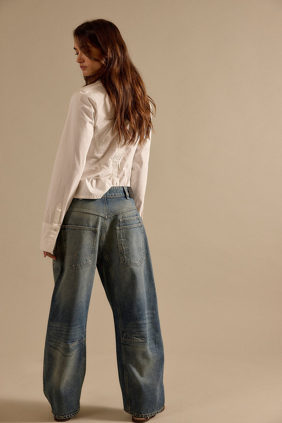 Woman wearing a white blouse and blue jeans against a beige background