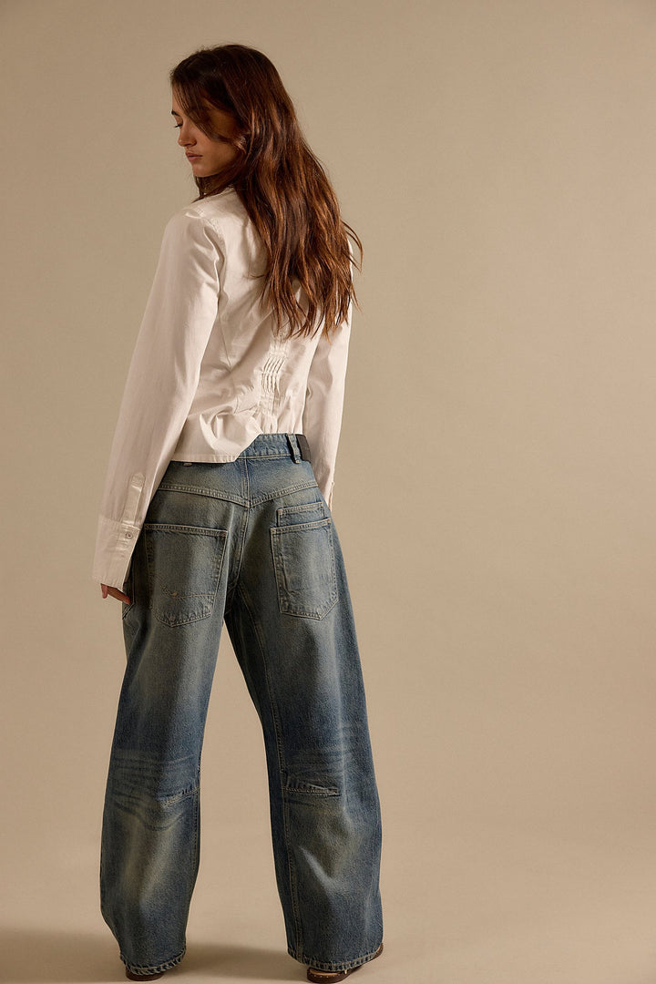 Woman wearing a white blouse and blue jeans against a beige background