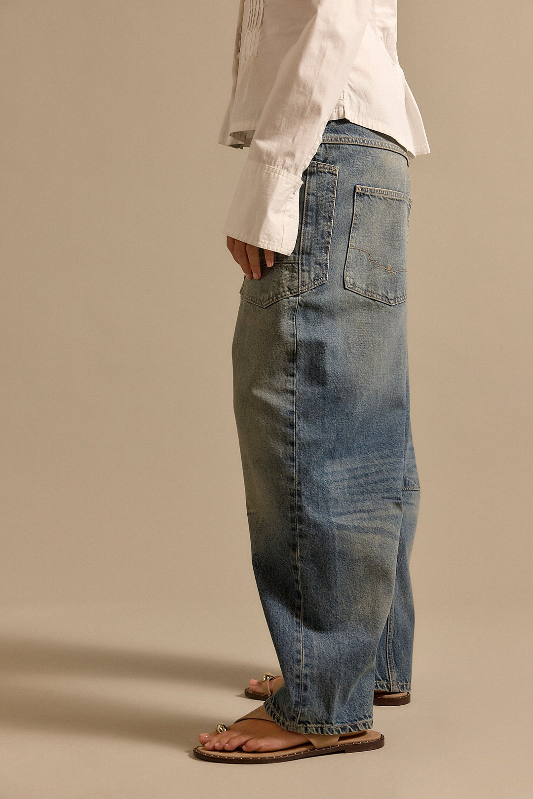Person wearing blue jeans and a white shirt on a beige background