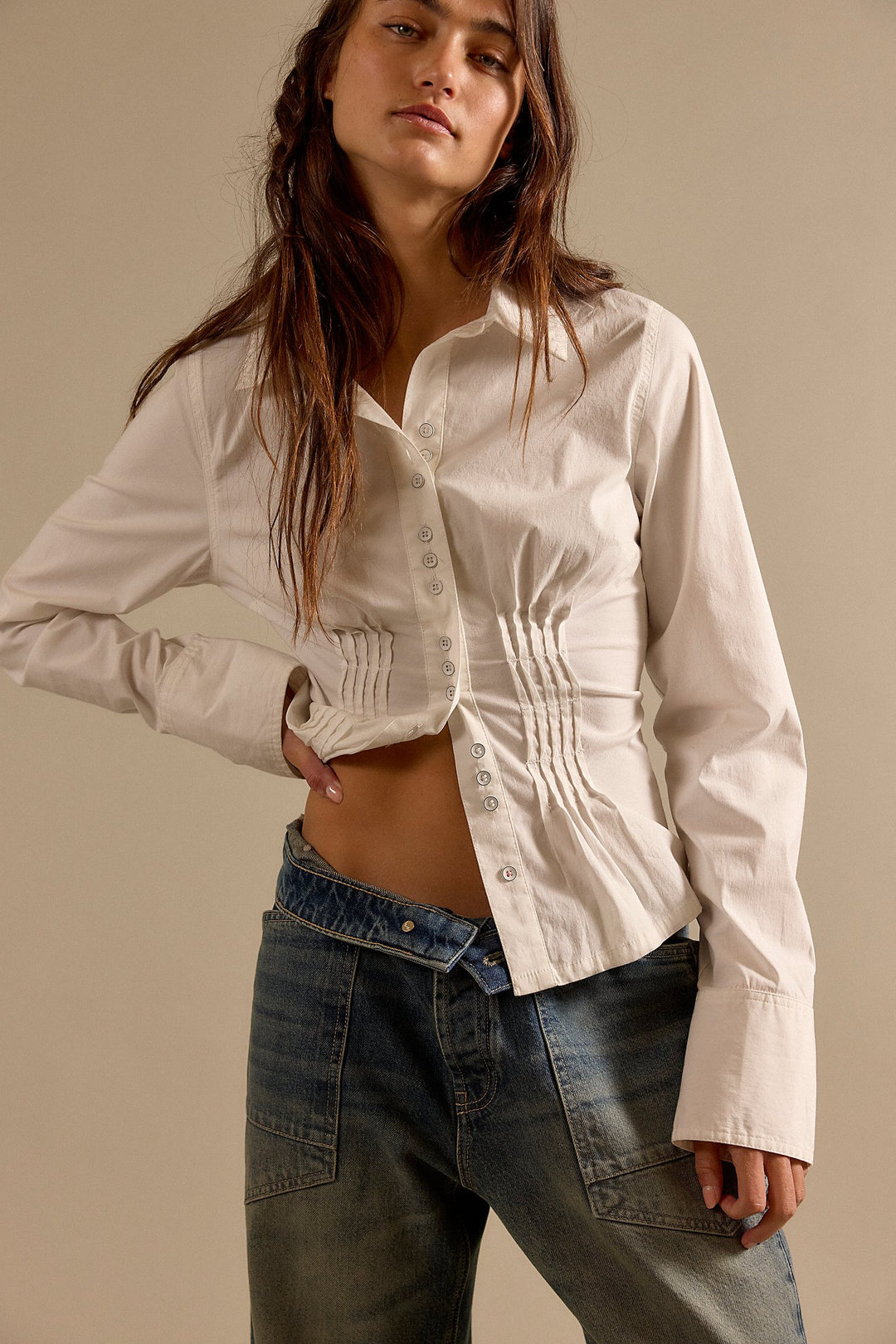 Woman wearing a white button-up shirt and blue jeans against a beige background