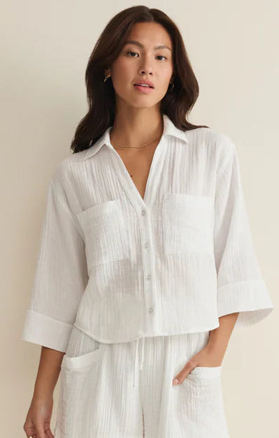 Woman wearing a white shirt and shorts set against a beige background