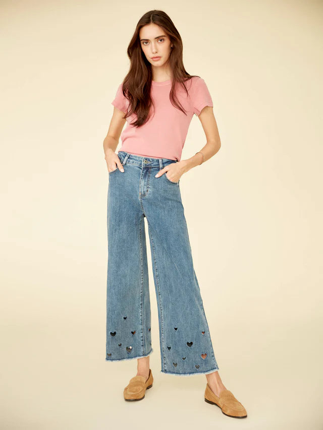 Woman wearing a pink top and blue jeans with heart embellishments on a beige background