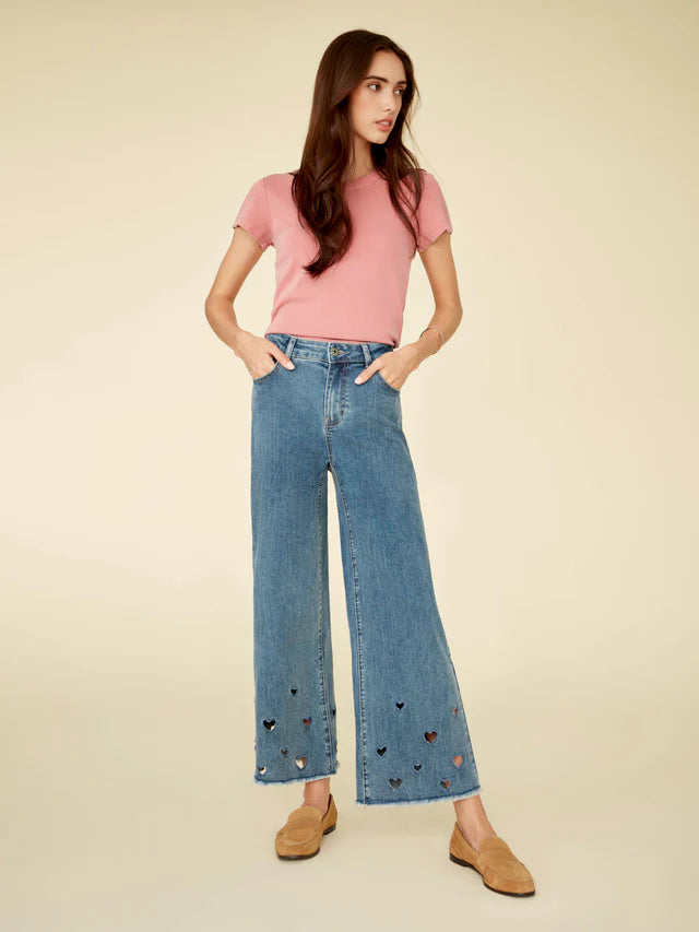 Woman wearing a pink top and blue jeans with heart cutouts on a beige background
