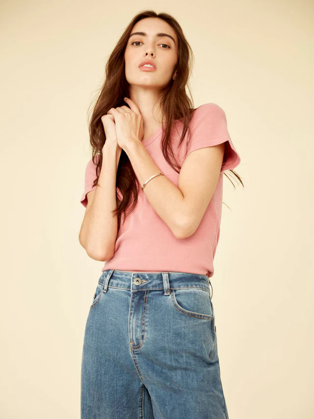 Woman wearing a pink top and blue jeans against a beige background
