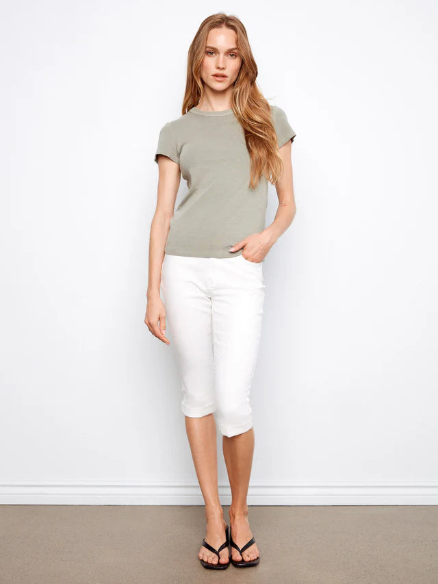 Woman wearing a green top and white pants against a white wall