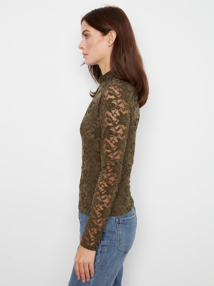 A woman shown in side profile wearing a fitted long-sleeve lace top in olive green and blue, paired with blue jeans, against a plain light gray studio background.