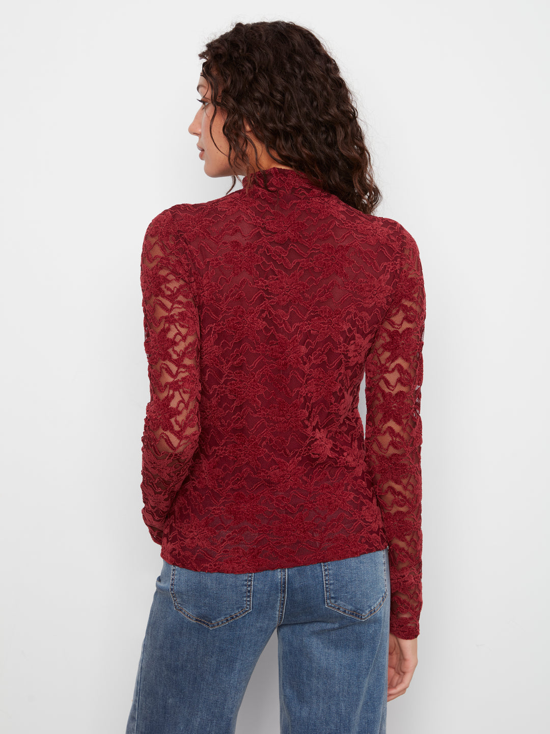 A woman shown from the back wearing a long-sleeve, high-neck burgundy lace top and blue jeans against a plain white background.