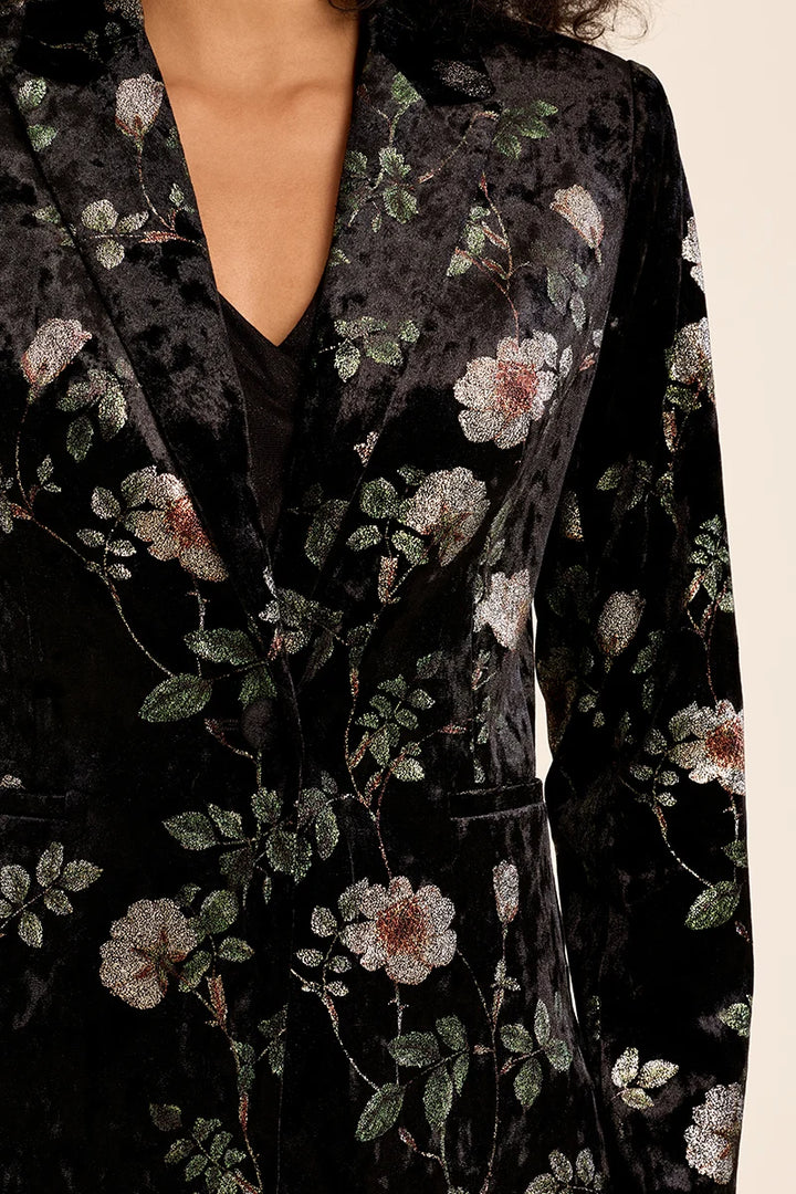 Close-up of a black velvet blazer with an intricate floral pattern featuring white, pink, and green embroidered flowers and leaves.