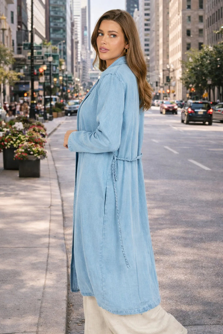 Woman in a long light blue denim dress standing on a city street.