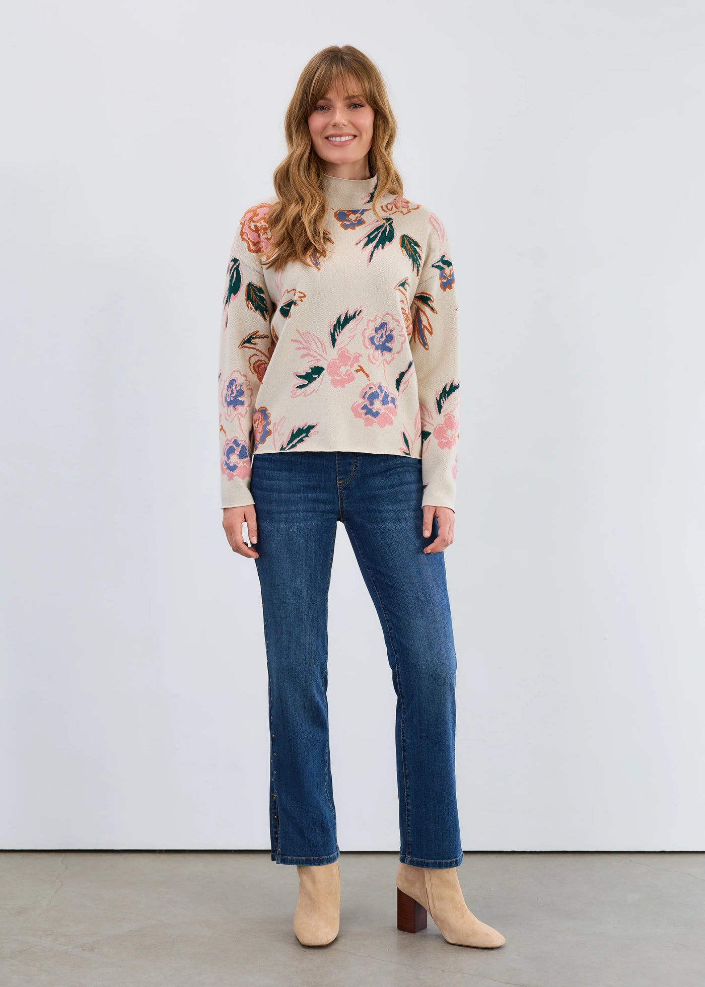 Woman wearing a floral sweater and jeans standing against a white background