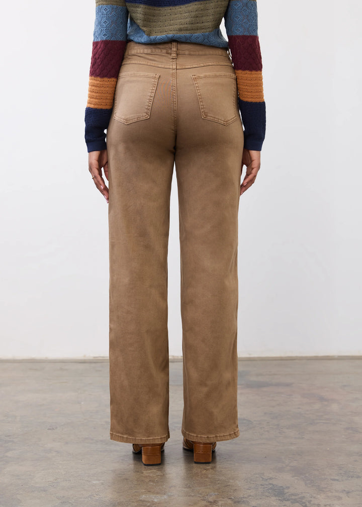 A person shown from the back wearing tan wide-leg pants, a multicolor striped sweater, and brown block-heel shoes in a studio setting.
