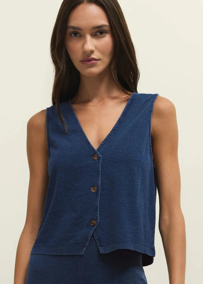 Woman wearing a blue sleeveless top with buttons on a beige background