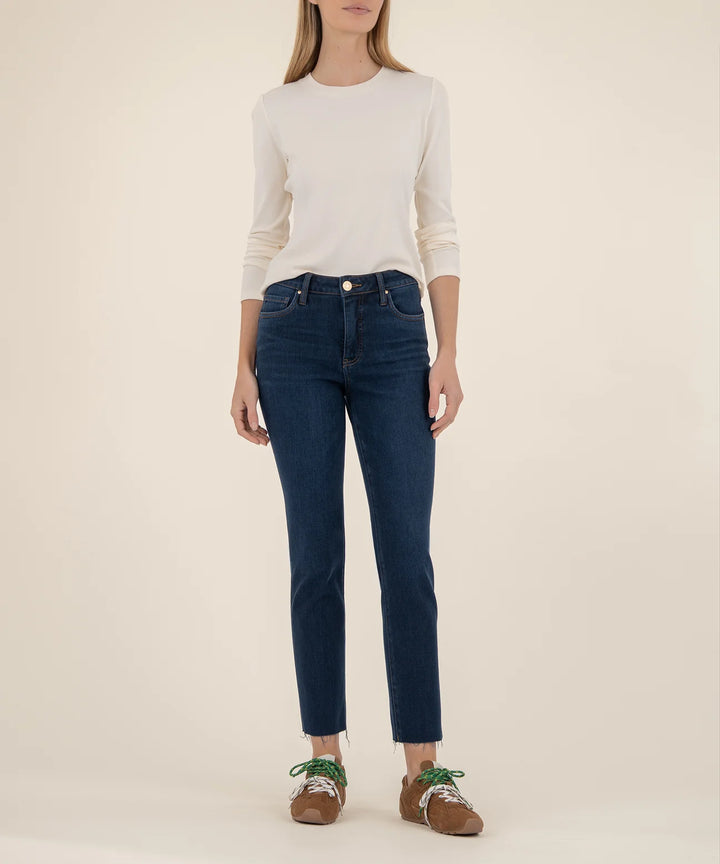 Person wearing dark blue jeans and a white sweater on a beige background