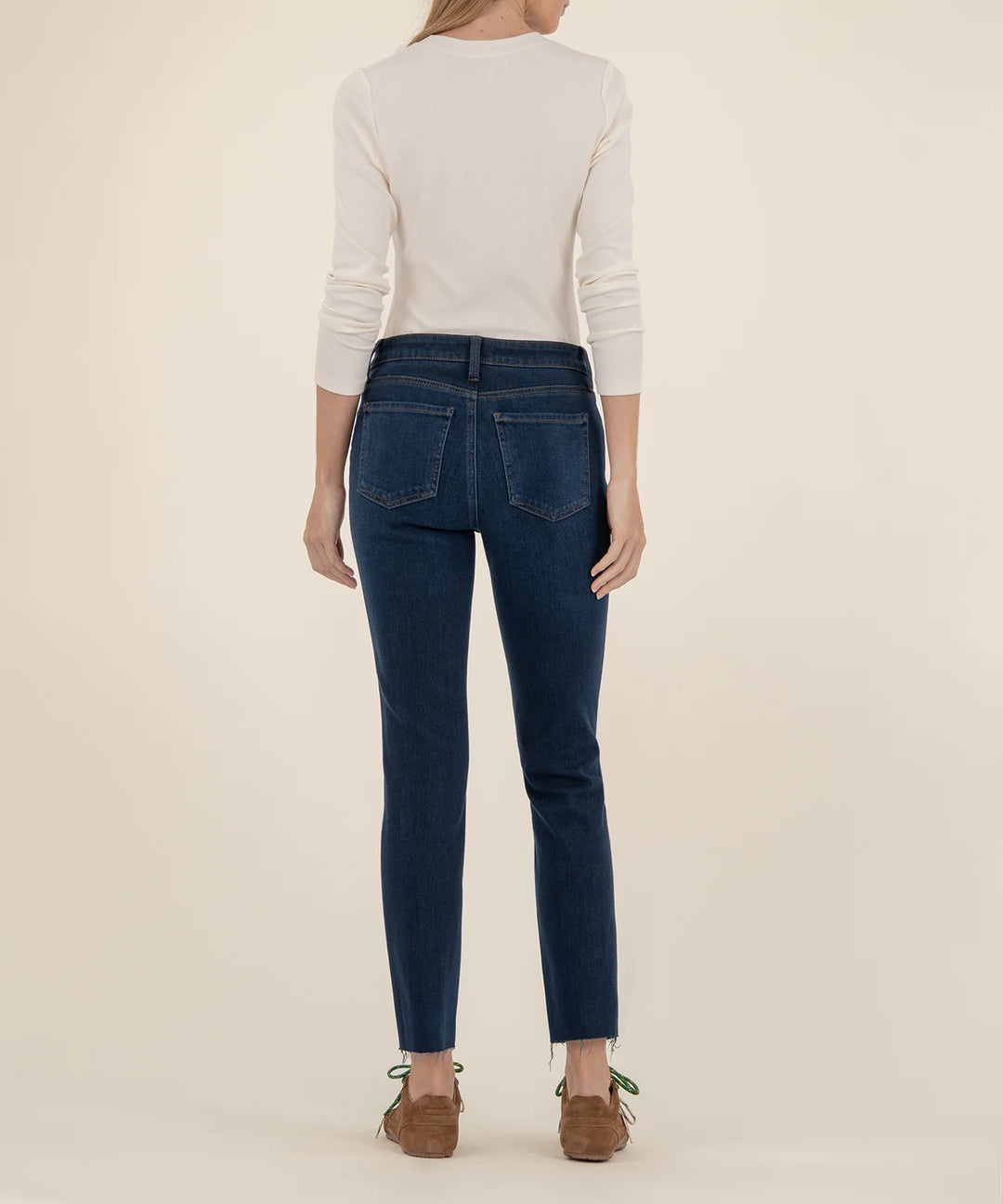 Person wearing blue jeans and a white sweater on a beige background