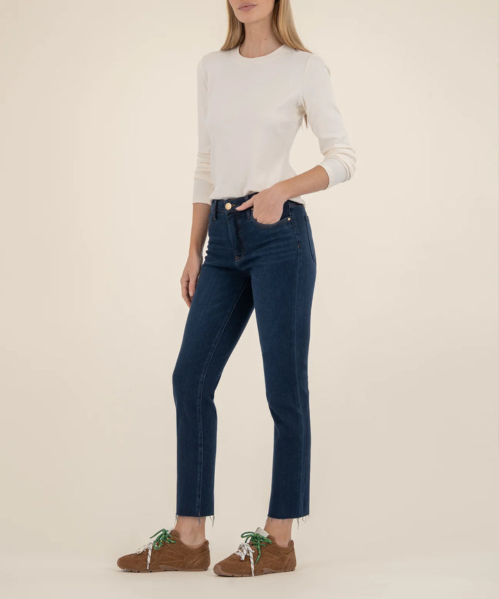 Person wearing a white long-sleeve top and dark blue jeans on a beige background