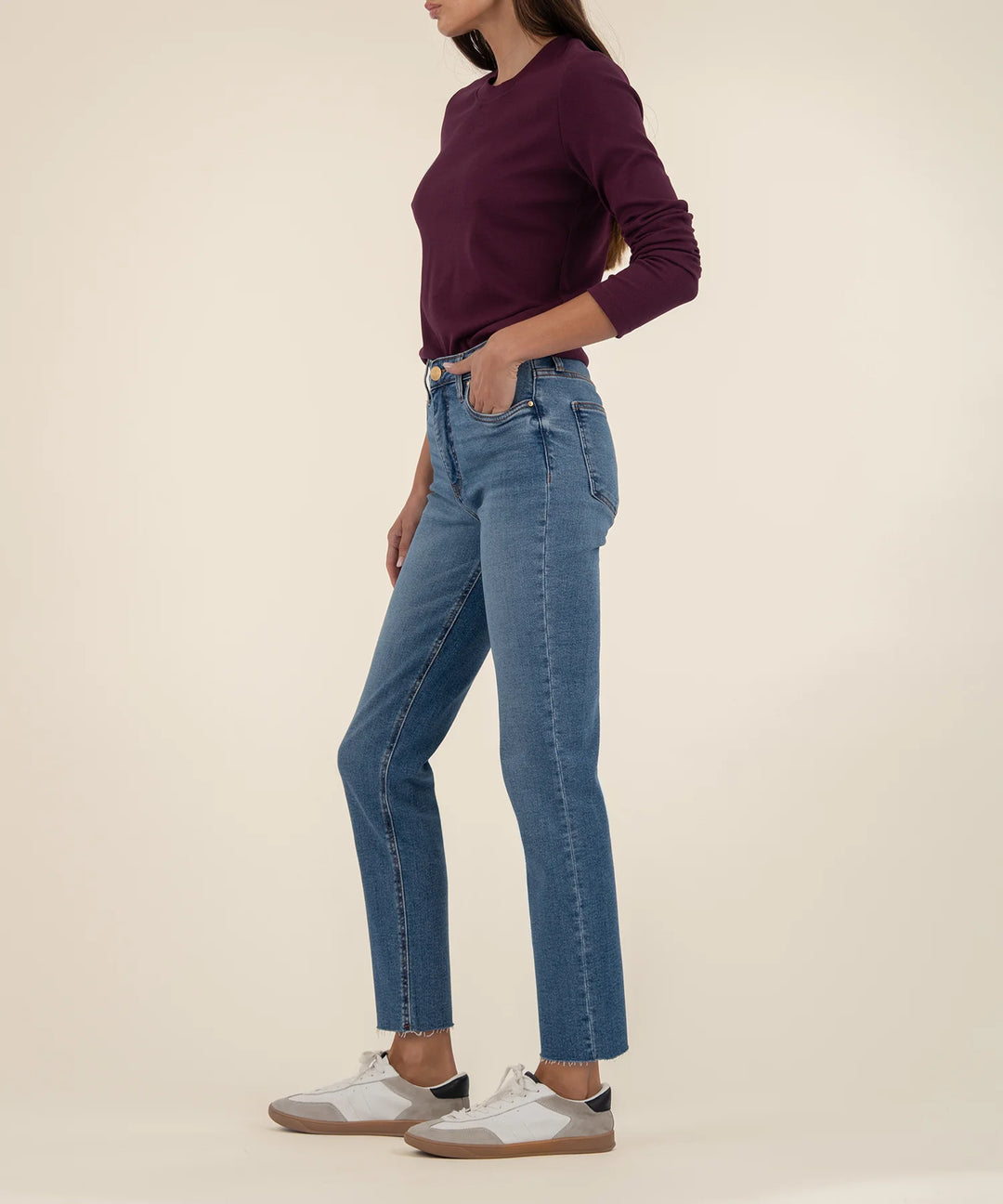 Person wearing a maroon sweater and blue jeans on a beige background