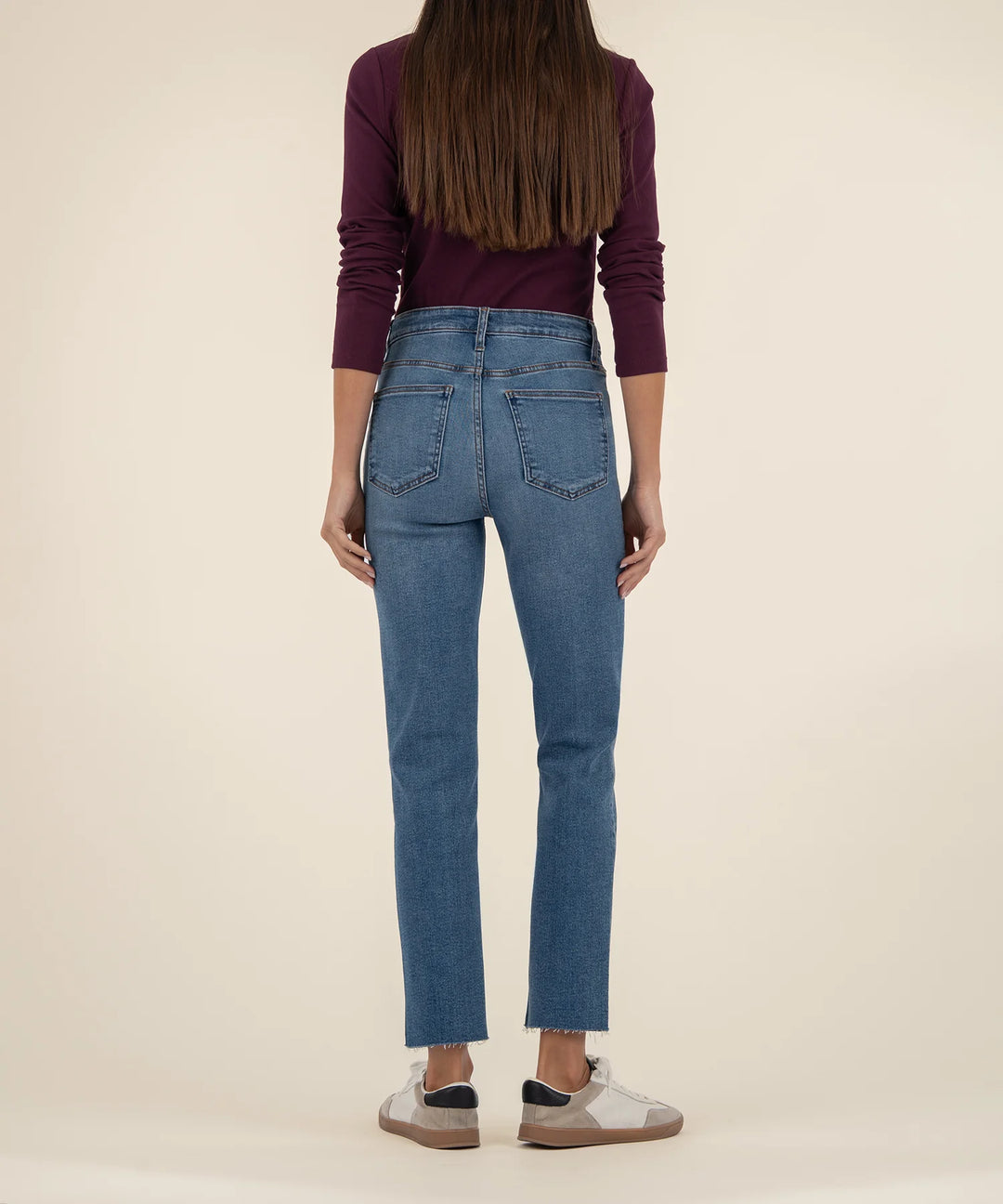 Person wearing blue jeans and a maroon top on a beige background