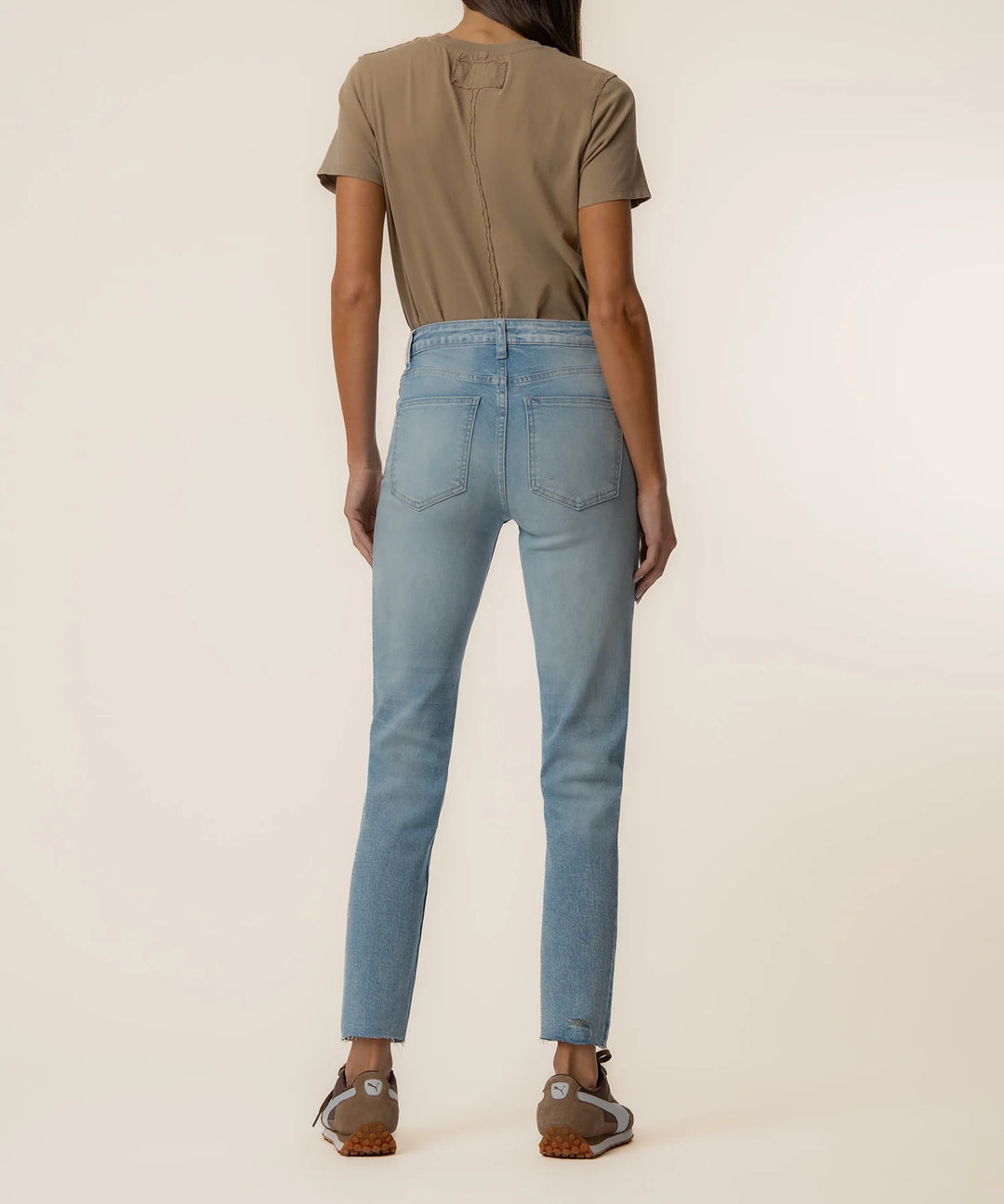 Person wearing light blue jeans and a brown shirt on a plain background
