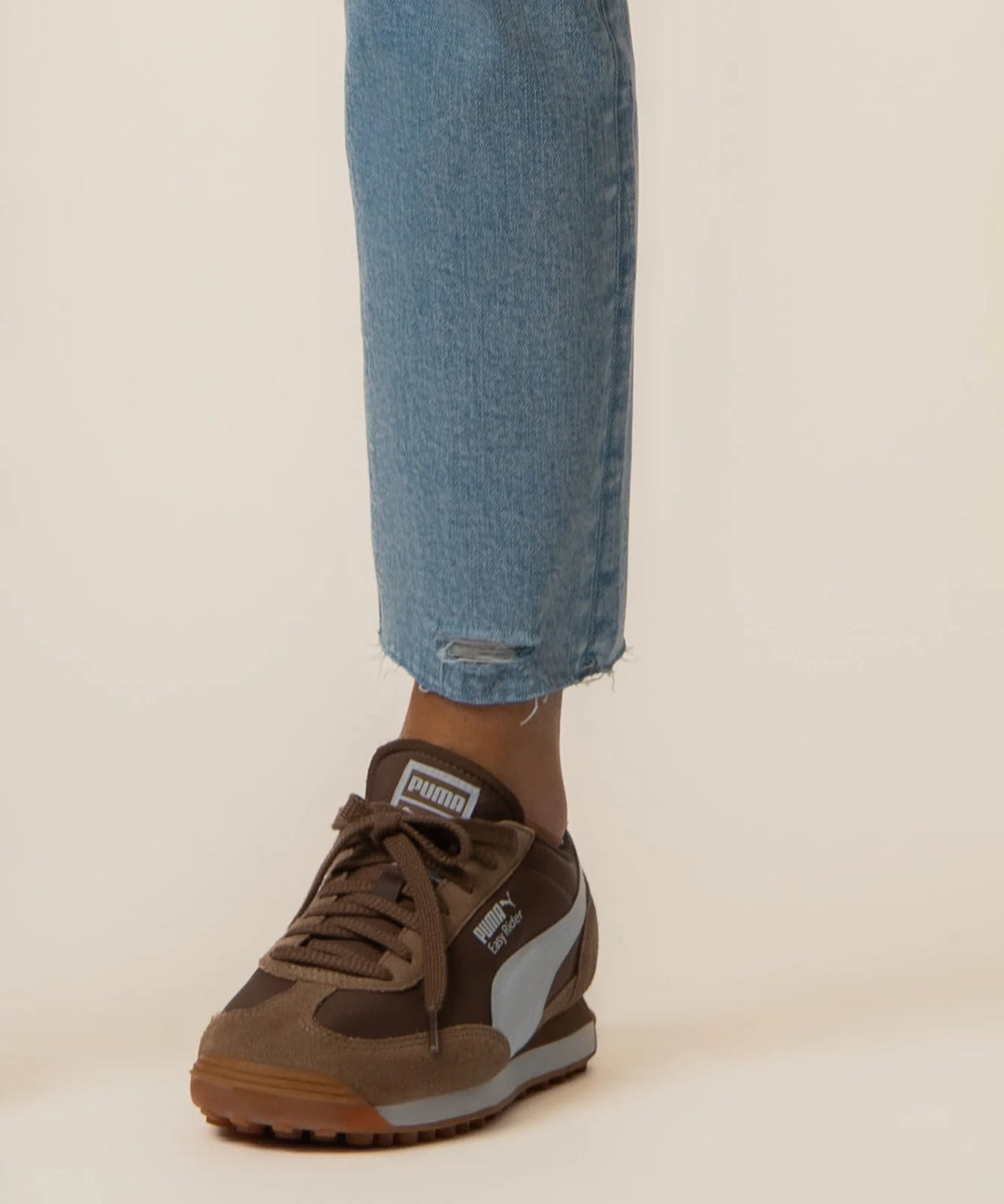 Brown Puma sneaker worn with blue jeans on a neutral background