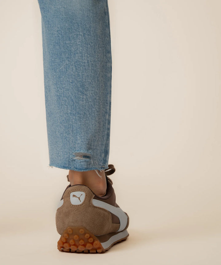 Brown suede shoe with orange sole worn with blue jeans on a beige background