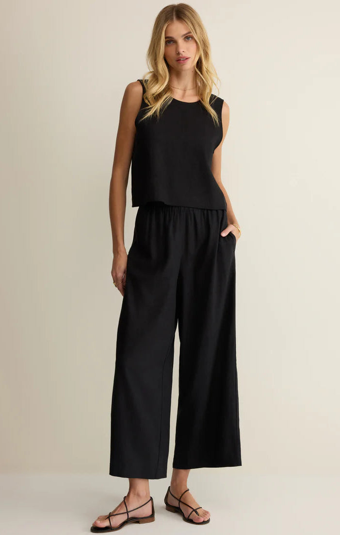 Woman wearing a black sleeveless top and wide-leg pants on a beige background