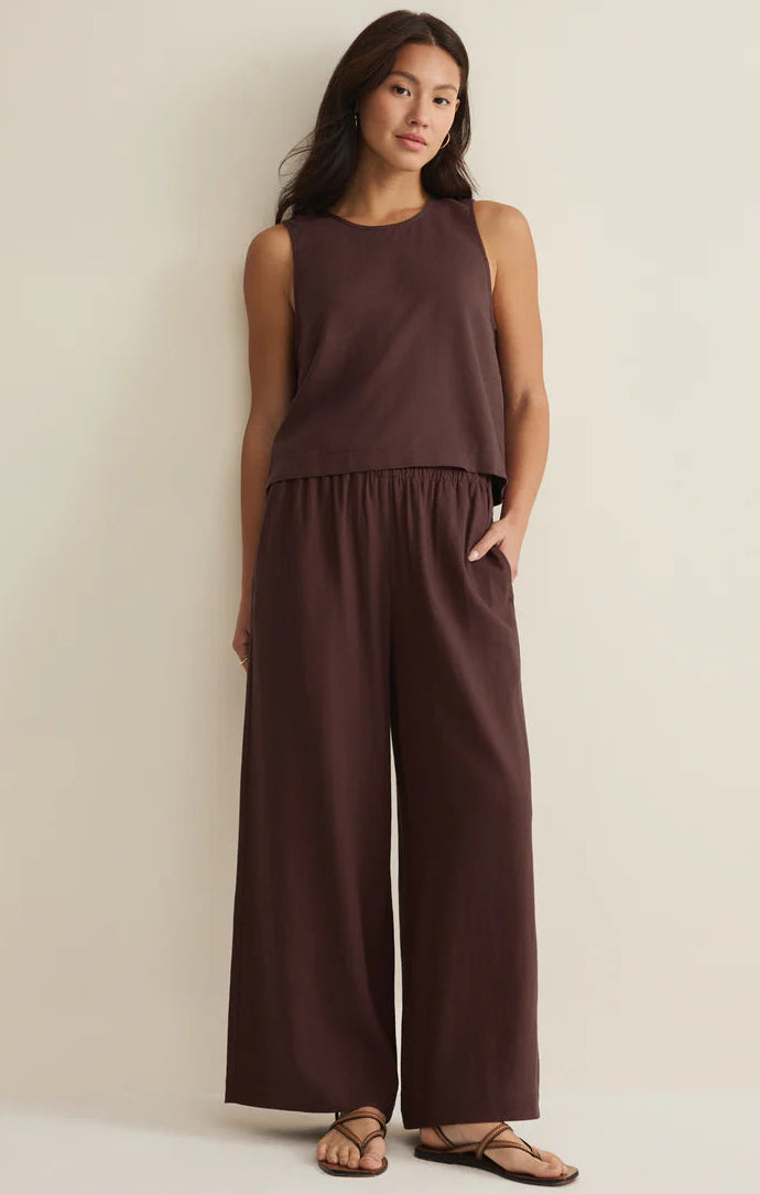 Woman wearing a brown sleeveless top and wide-leg pants against a beige background