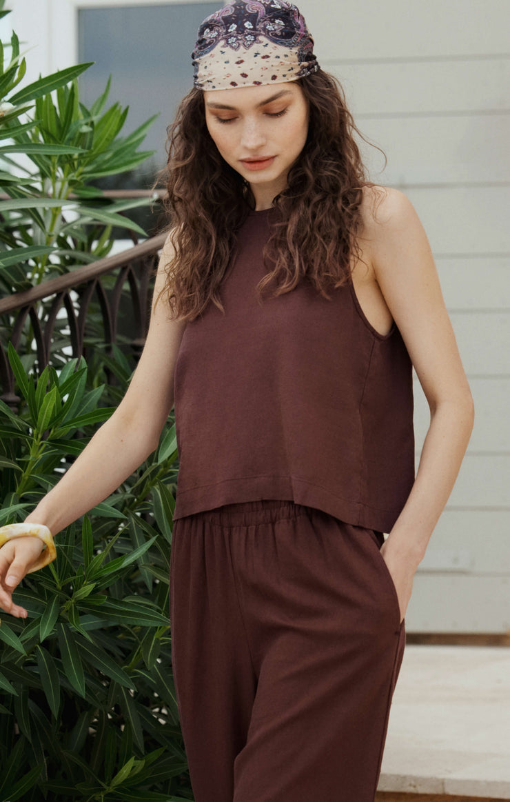 Woman wearing a brown sleeveless top and pants with a headscarf, standing outdoors.