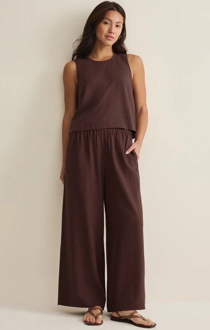Woman wearing a brown sleeveless top and wide-leg pants against a beige background