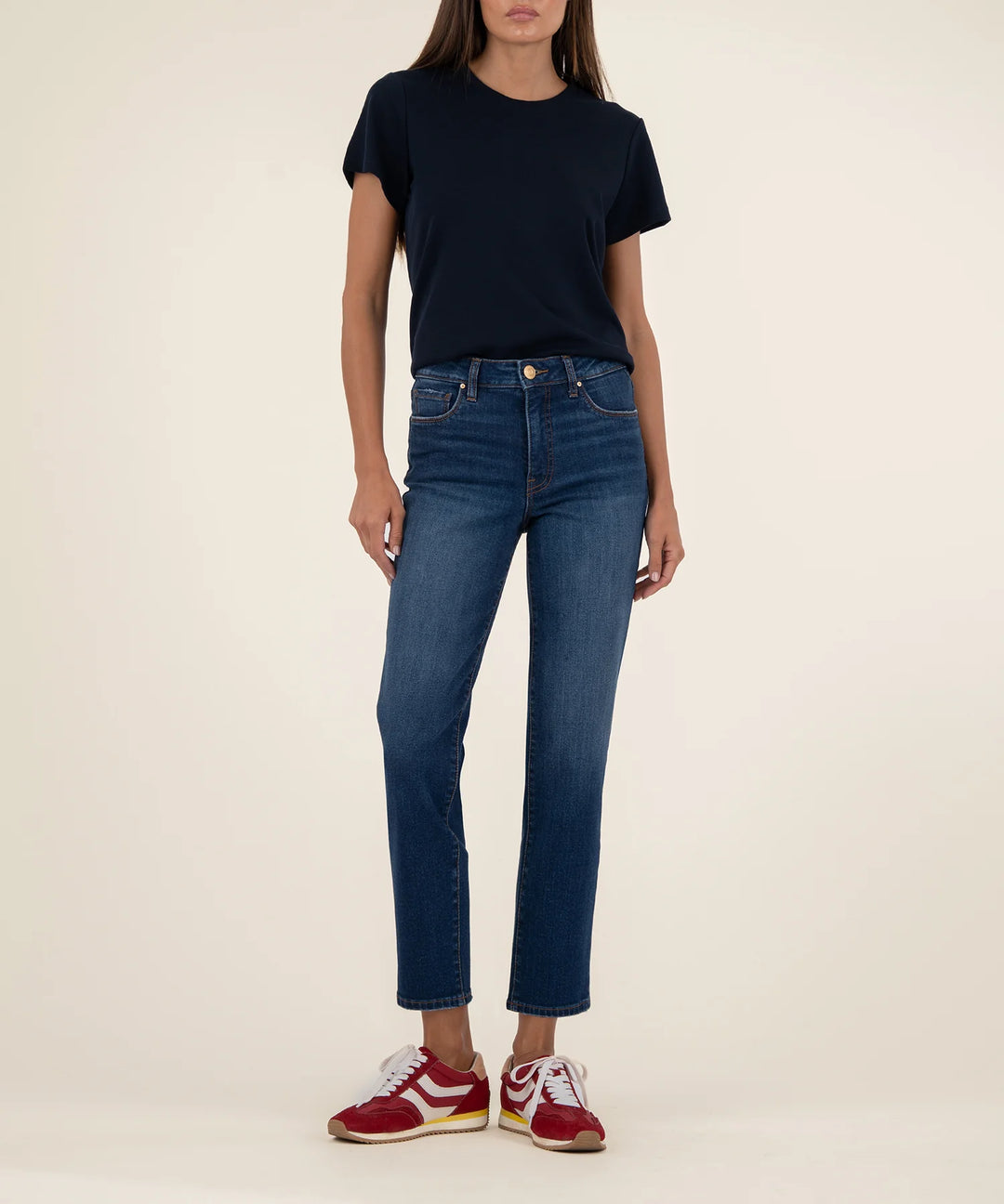 Person wearing a black t-shirt and blue jeans with red and white sneakers on a beige background