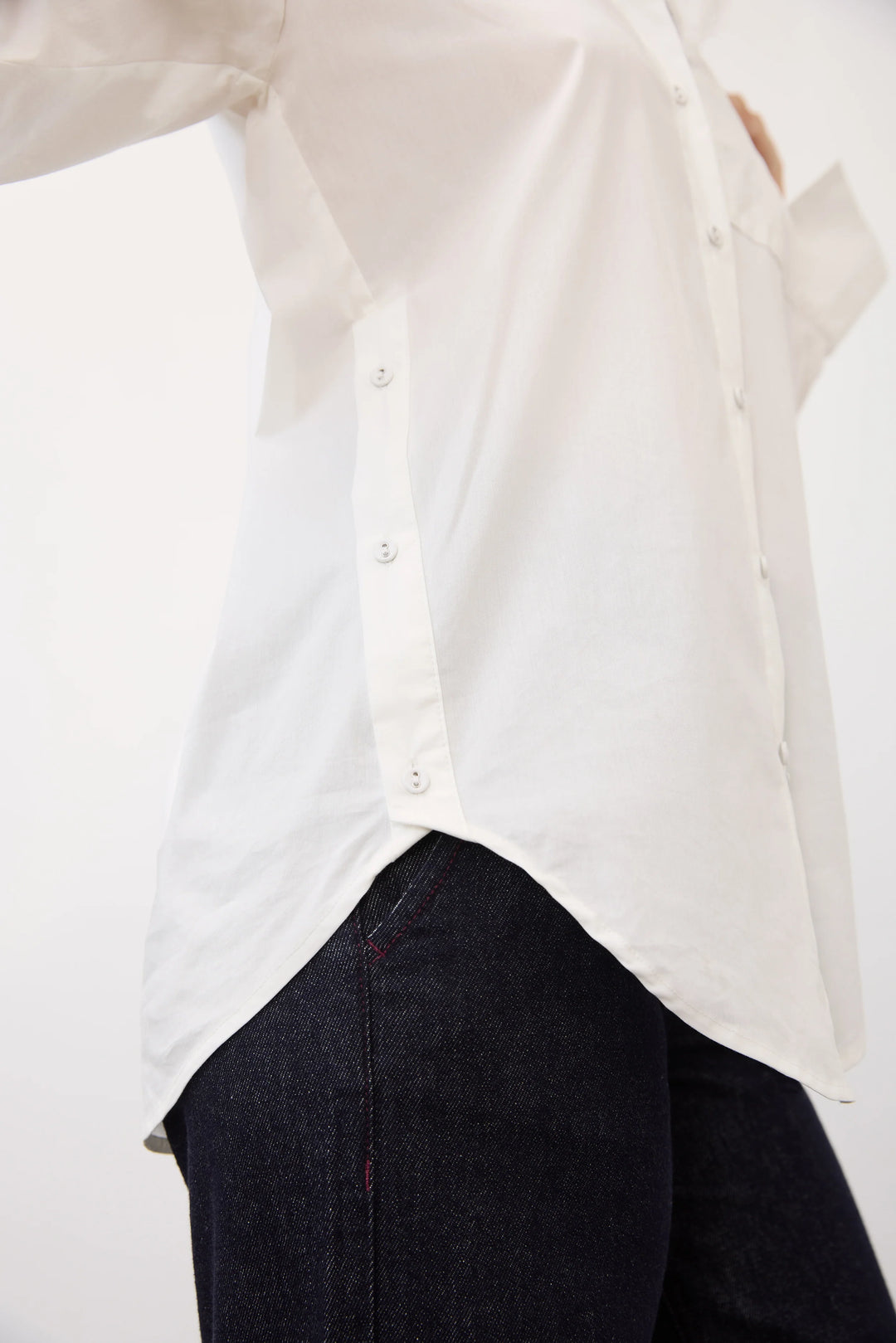 A close-up of a person wearing a white button-front shirt tucked into dark navy jeans, cropped from the chest down against a plain light background.