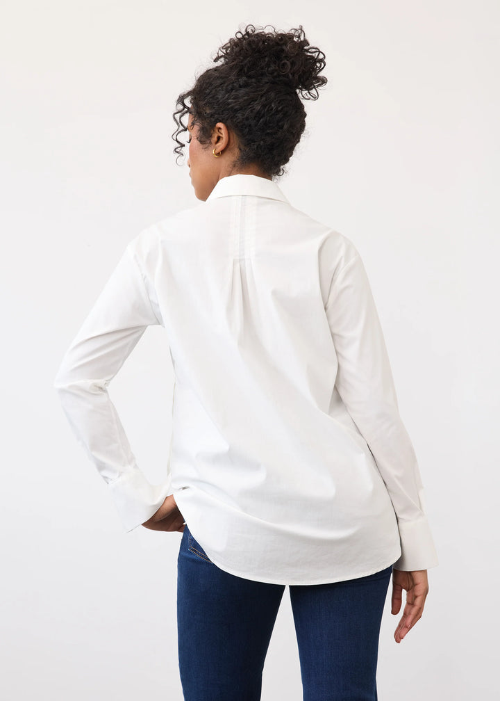 A woman shown from the back wearing a white long-sleeve button-up shirt and dark blue jeans against a plain white studio background.