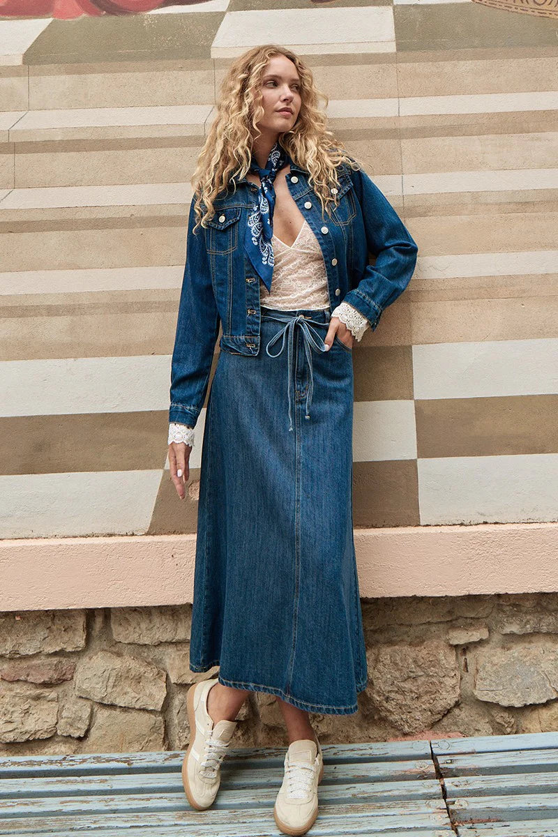 Woman wearing a denim outfit standing on steps with a striped wall background