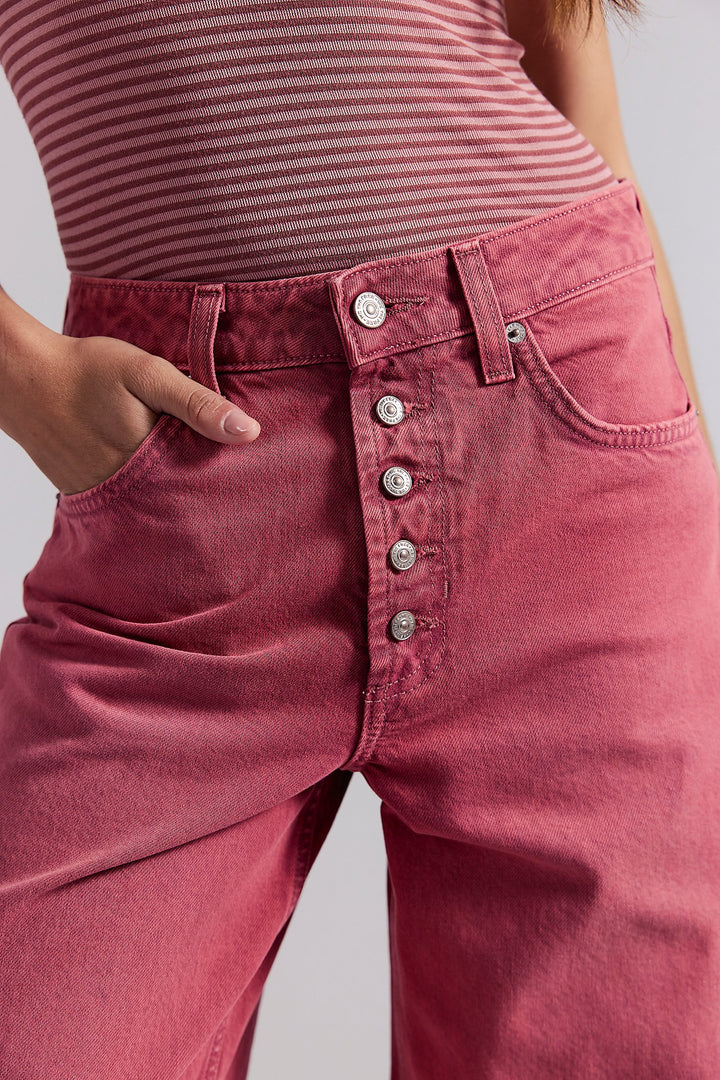 Close-up of pink jeans with button details on a plain background