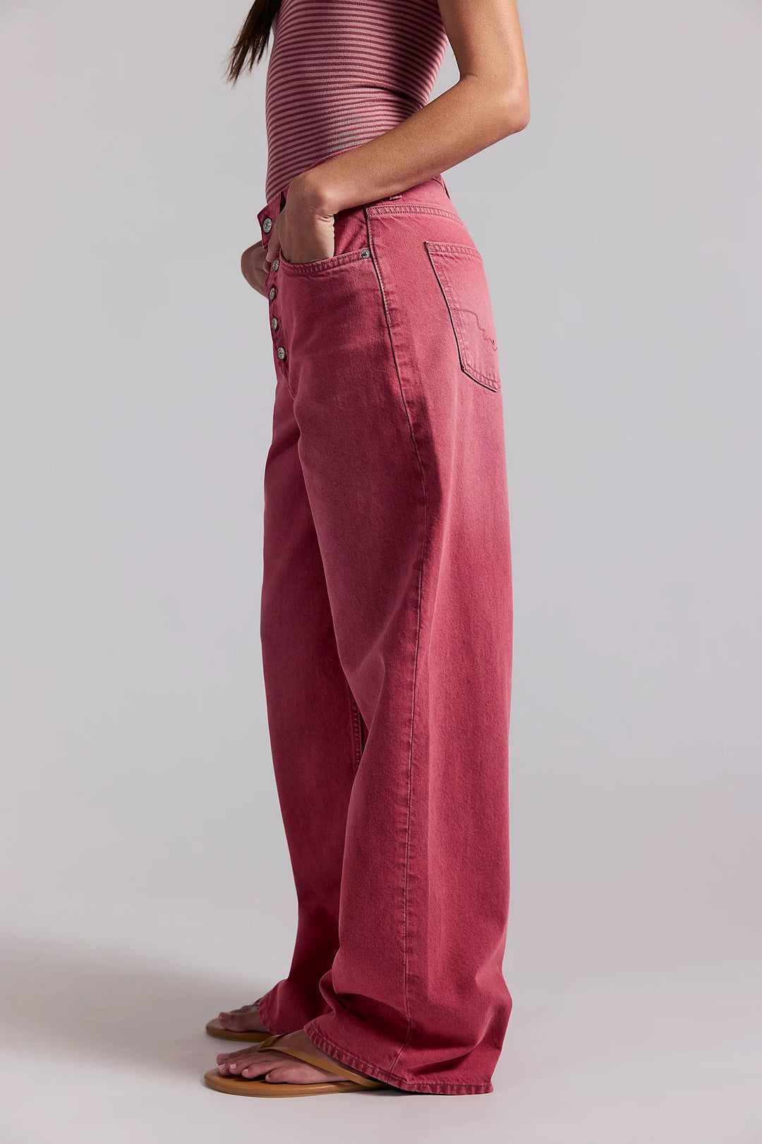 Person wearing pink wide-leg jeans and a matching top on a plain background