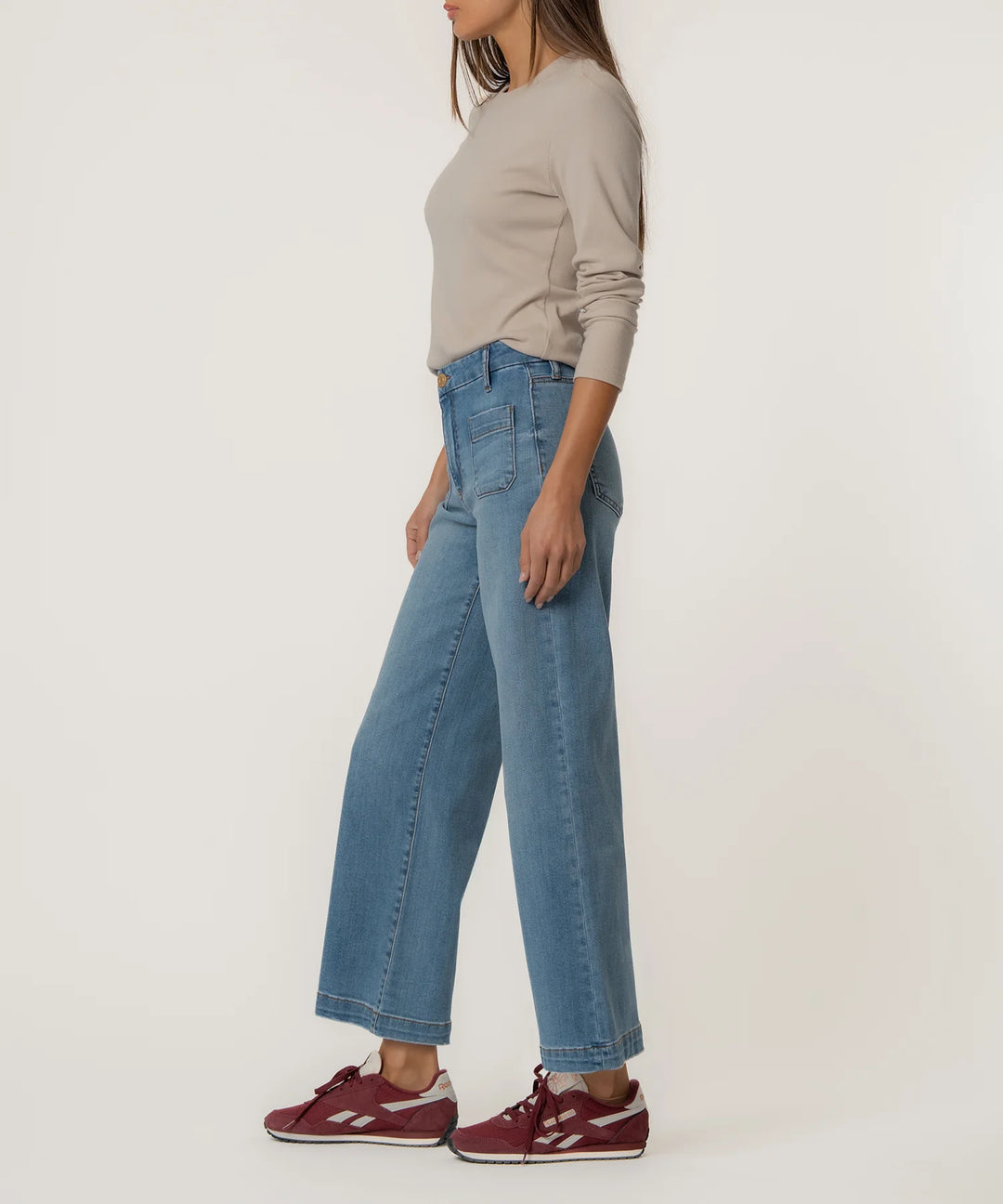 Person wearing blue jeans and a beige top on a white background