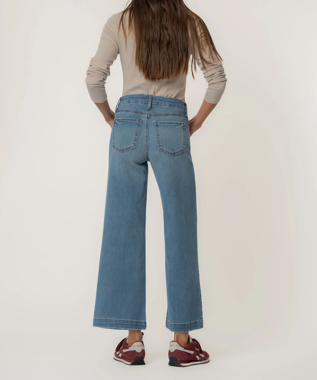 Person wearing blue jeans and a beige top on a plain background