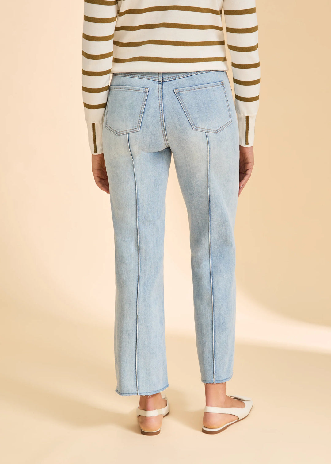 Person wearing light blue jeans and a striped sweater on a beige background