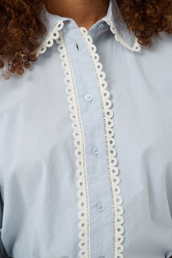 Light blue shirt with white lace trim worn by a person with curly hair.