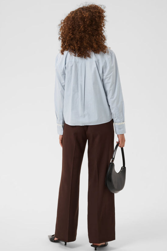 Person wearing a light blue shirt and brown pants holding a black handbag on a white background
