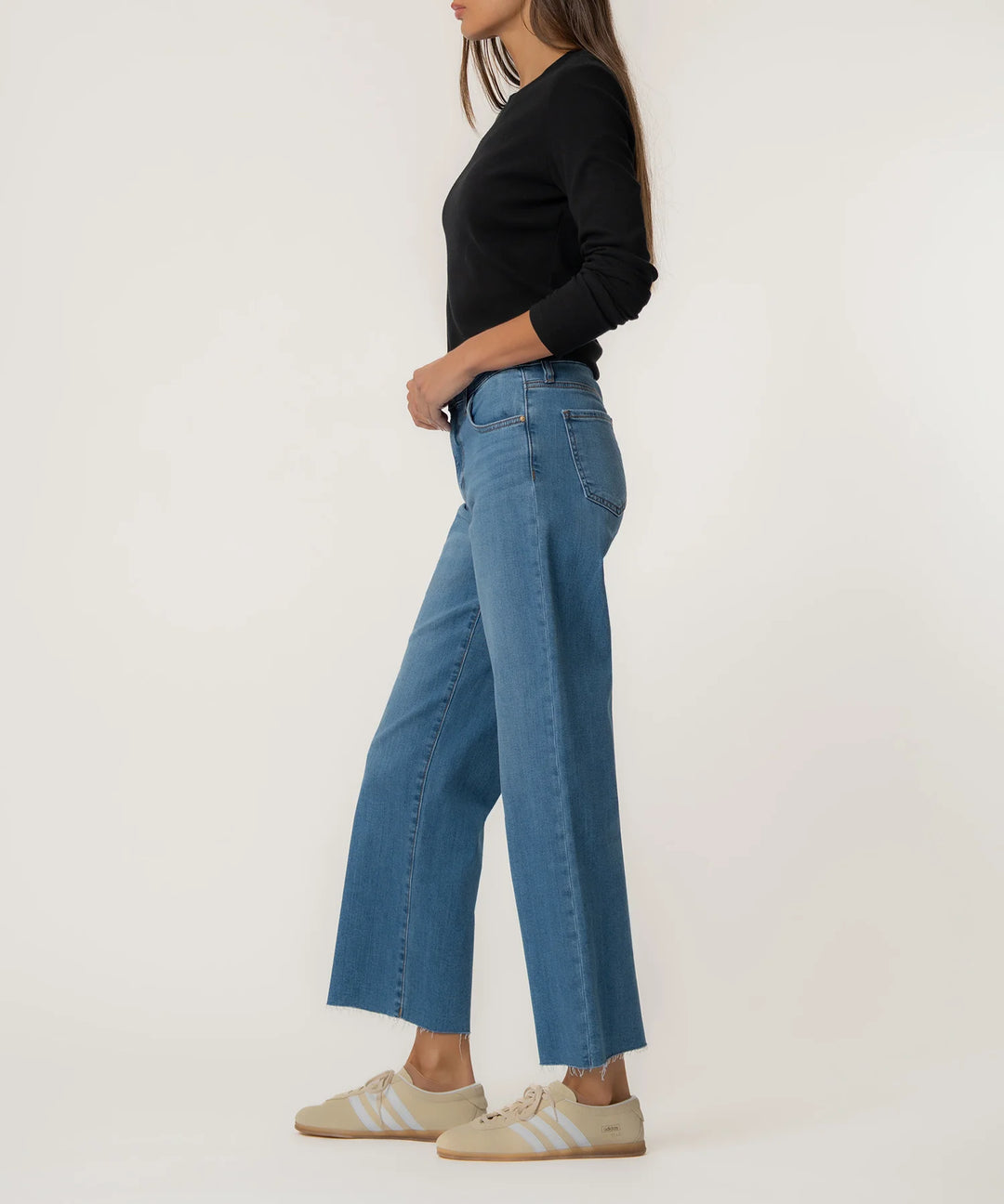 Person wearing blue jeans and a black top on a white background