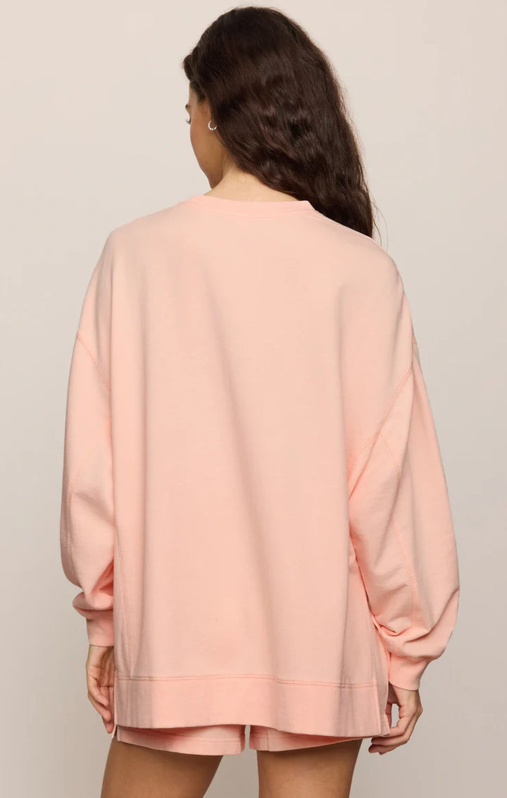Person wearing a light pink oversized sweatshirt and shorts set on a plain background