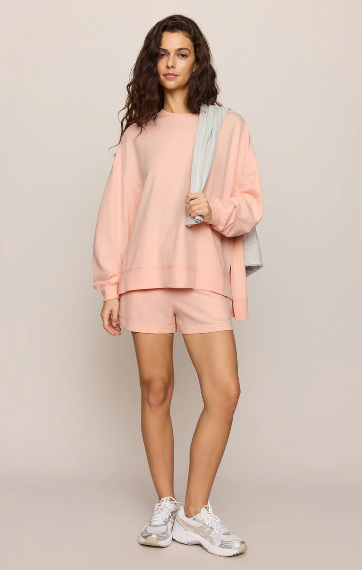 Woman wearing a pink outfit with shorts and a sweatshirt on a beige background