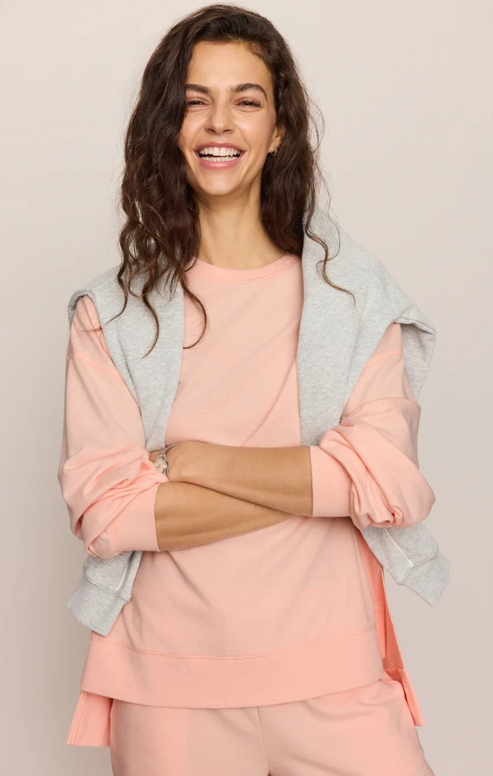 Woman wearing a pink outfit with a gray cardigan against a beige background