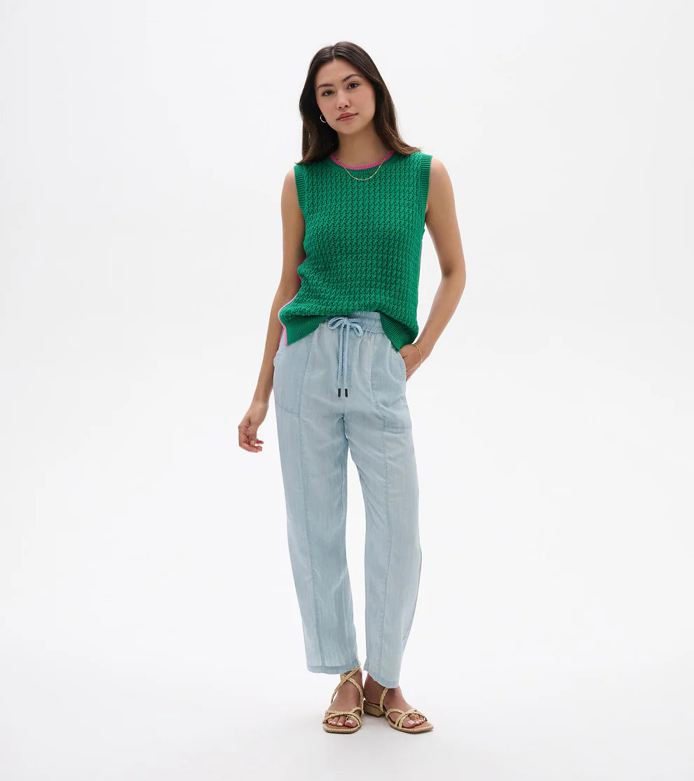 Woman wearing a green sleeveless top and light blue pants on a white background
