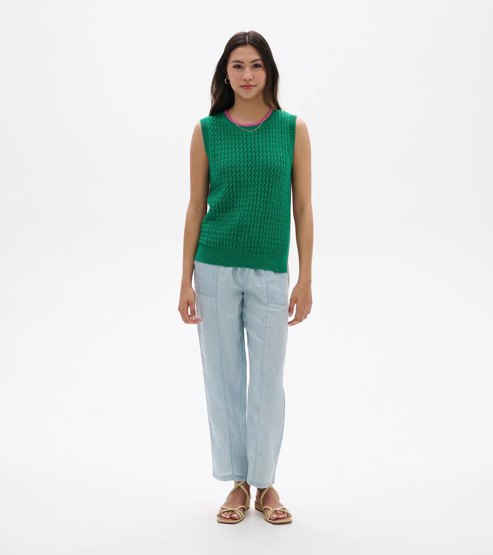 Woman wearing a green sleeveless top and light blue pants on a white background