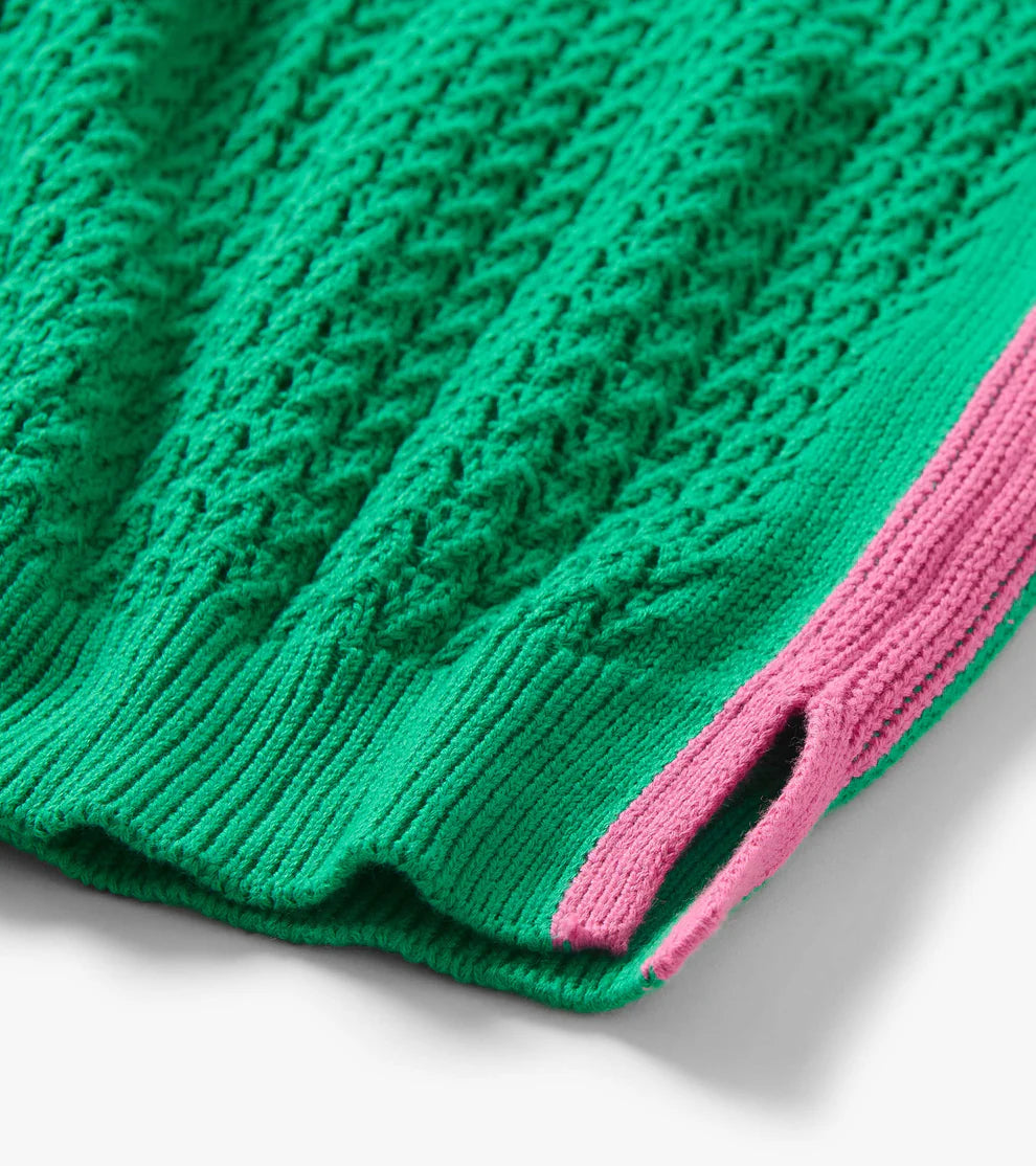 Close-up of a green knitted garment with pink trim on a white background