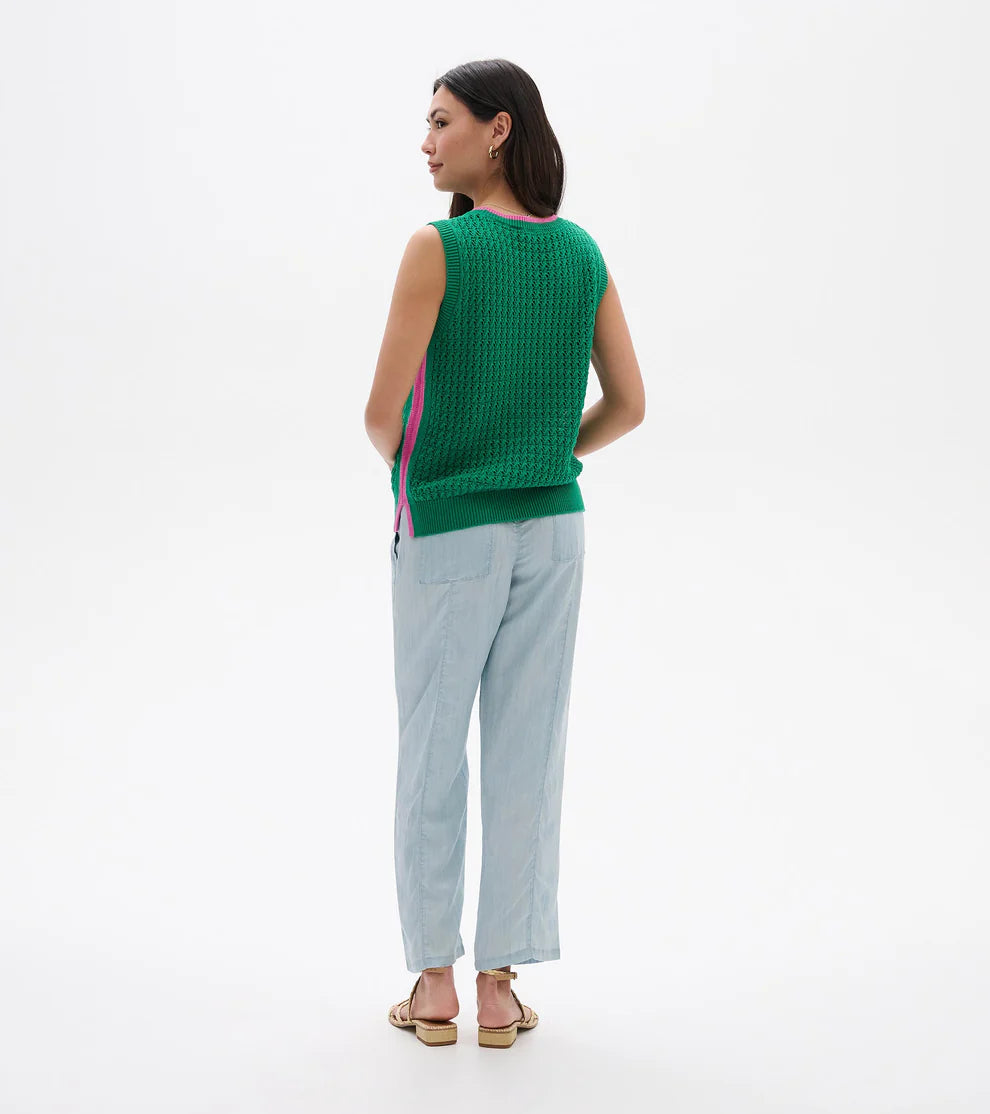 Woman wearing a green sleeveless top and light blue pants on a white background