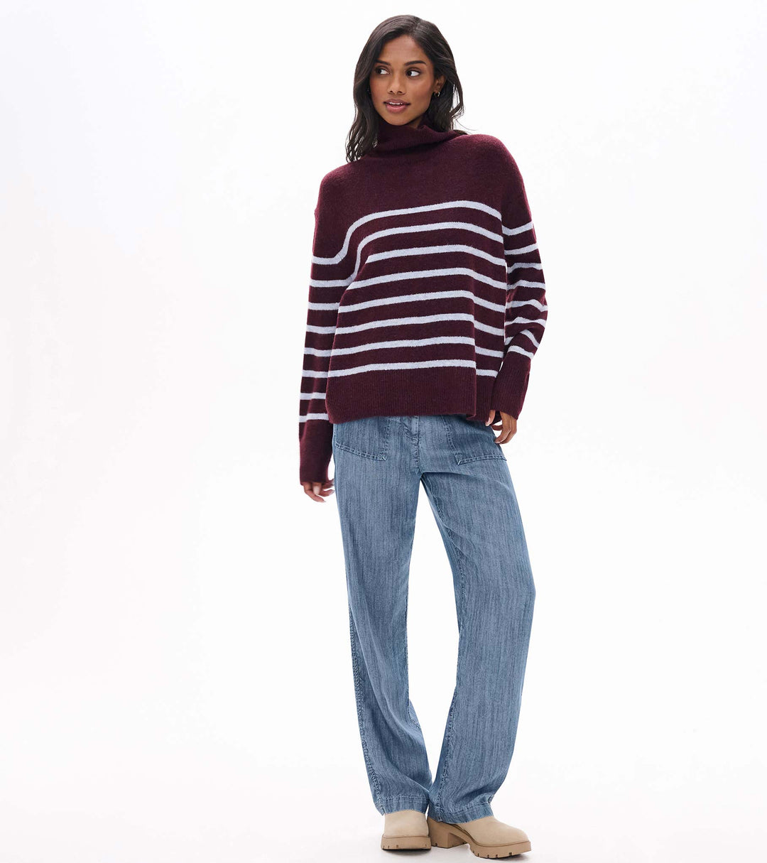 Woman wearing a maroon and white striped sweater with blue jeans on a white background