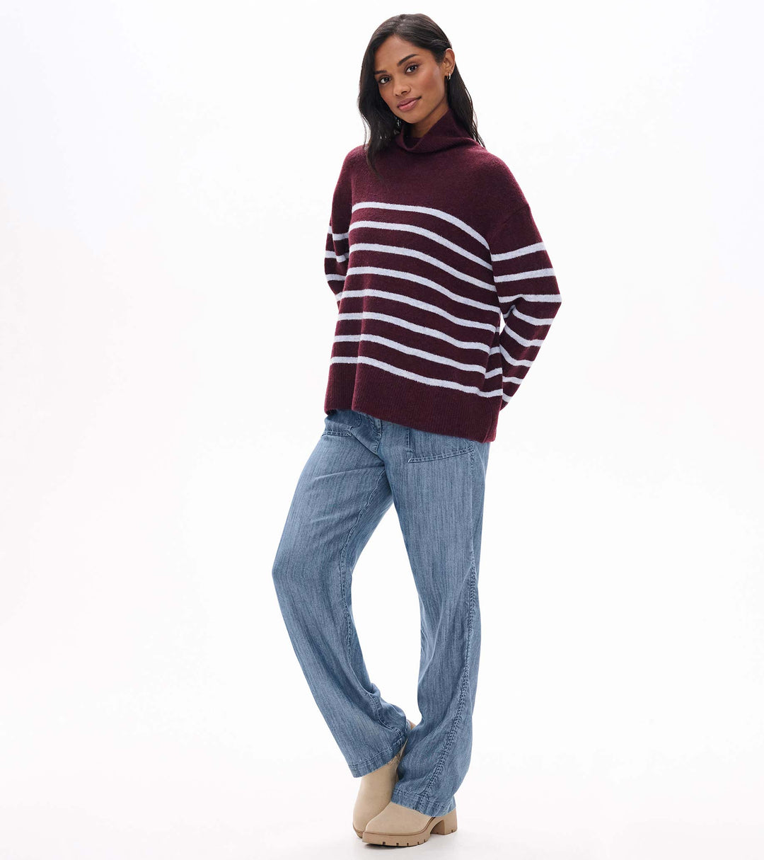 Woman wearing a maroon and white striped sweater with blue jeans on a white background