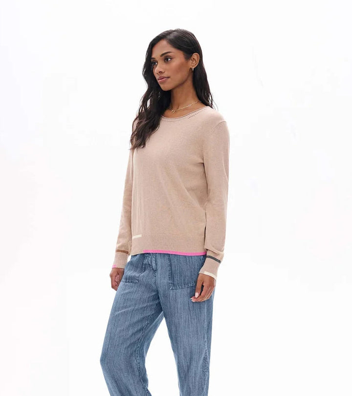 A woman modeling a light beige knit crewneck sweater and wide-leg blue jeans against a plain white studio background.